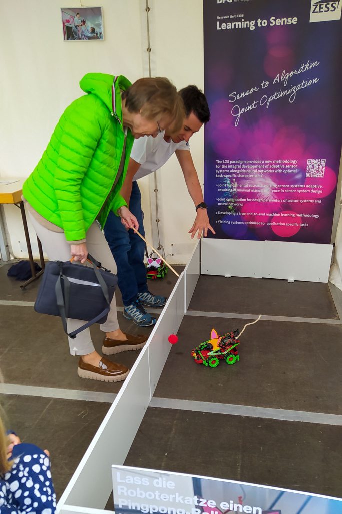 Rector Prof Stefanie Reese working with an AI robotic cat at ZESS and DFG research unit "Learning to Sense" during Open University 2025. [Photo: Sarah Wagener/Uni Siegen]